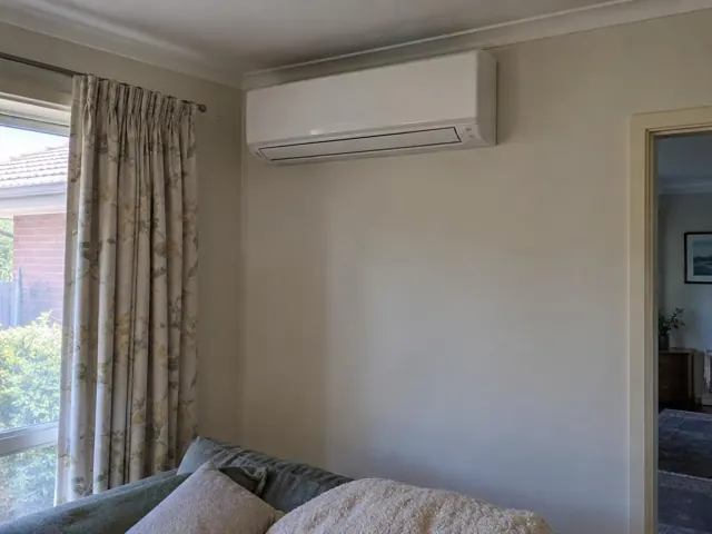 Wall-mounted split system above a sofa in a beige living room with curtains in Edwardstown